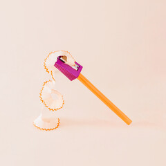 Creative composition made of orange color pencil and purple pencil sharpener against a bright beige background. Minimal back to school concept.