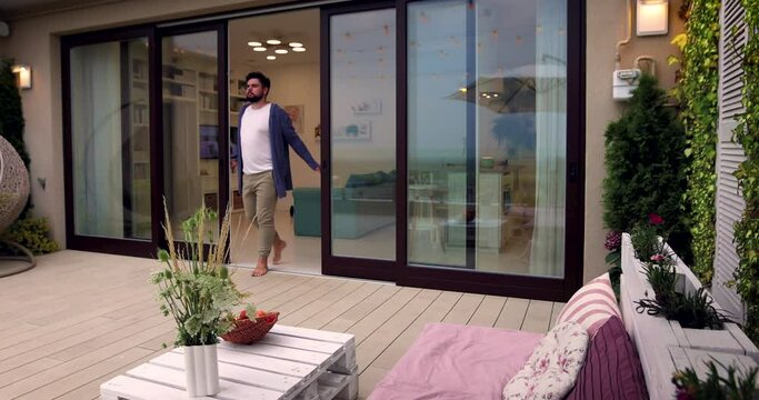 man opens wooden sliding doors, going out on rooftop patio with cozy lounge zone