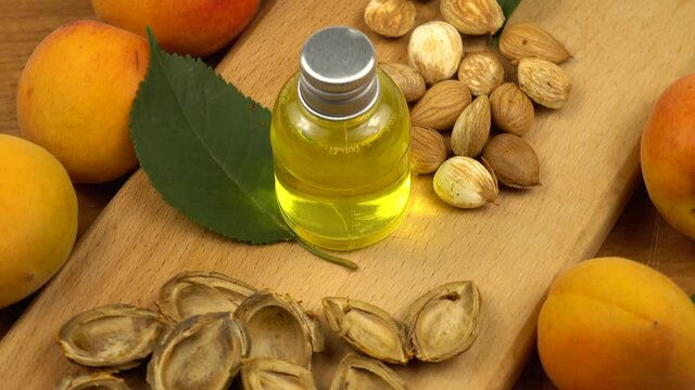 A bottle of the apricot kernel oil stands on a wooden board among the fresh apricots and the apricot kernels. Apricots and their products as a skin care product.