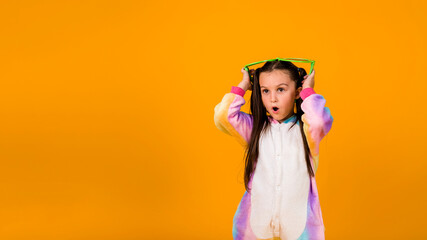 a surprised girl in a plush jumpsuit and large glasses on a yellow background with a place for text