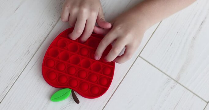 figers of toddler kid are pushing the bubbles on sensory toy, trendy pop it fidget toy in apple shape