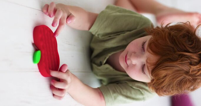 vertical video of a smiling boy playing with colorful sensory toys. pushing the bubles on pop it fidget toy