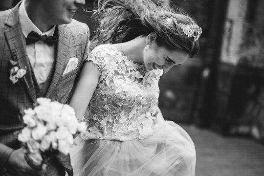 Stylish happy bride and groom walking on background of old church in rain, close up. Provence wedding. Beautiful emotional wedding couple smiling. Romantic moment, black and white image