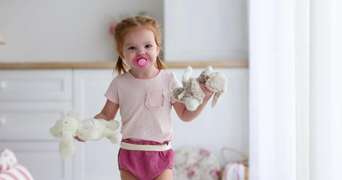 cheerful baby girl with toys and pacifier running around the living room at home