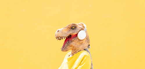 woman with dinosaur mask on a yellow background listens to music