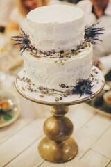Stylish rustic wedding cake with lavender and thistle decor on vintage stand on table at wedding...