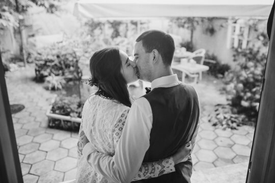 Stylish bride and groom gently embracing in stylish restaurant. Beautiful romantic wedding couple kissing, back view. Provence wedding reception. Black and white photo
