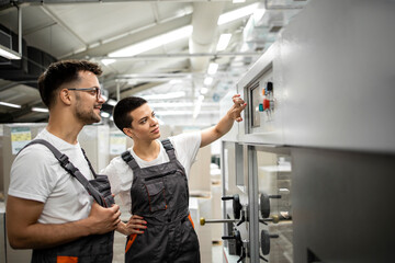 Experienced technician training new worker to operate industrial machine in factory.