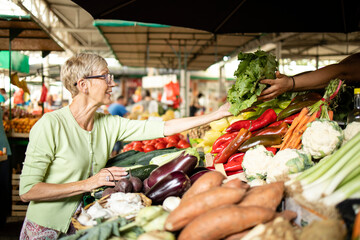 Senior woman buying fresh organic vegetables at market place for healthy nourishment.