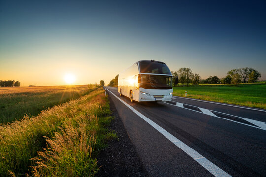 White bus traveling on the asphalt road in rural landscape at sunset