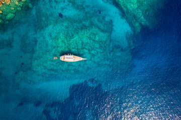 Fototapeta na wymiar Aerial top down view of a sailing boat anchored on a emerald reef in the turquoise sea