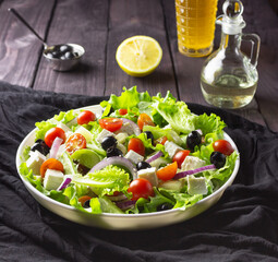 Greek salad in a plate on a dark background. Healthy vegetarian food. Feta cheese, lettuce leaves, cherry tomatoes.
