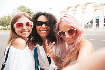 Three young beautiful smiling hipster female in trendy summer clothes.Sexy carefree multiracial women posing on the street background.Positive models having fun in sunglasses. Taking Pov selfie