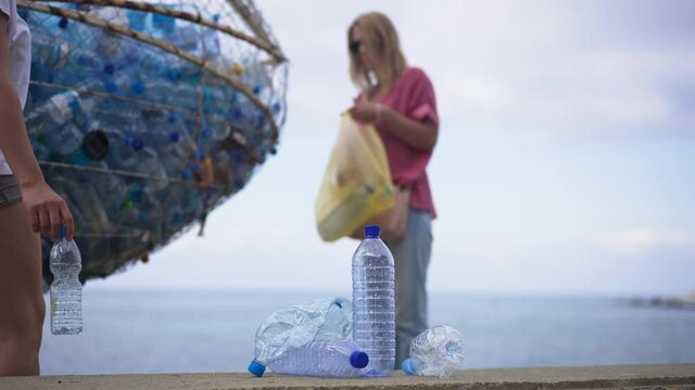 Blurred woman putting plastic waste in special place on beach coast as unrecognizable millennial passing at front leaving empty bottle aside. Lifestyle and environment concept