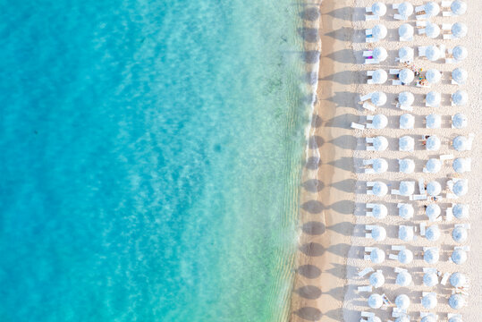 View from above, stunning aerial view of a white sand beach bathed by a turquoise water and relaxed people under some beach umbrellas at sunset. Cala di volpe beach,Sardinia, Italy.