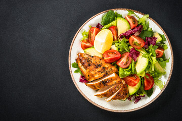Healthy salad with leaves, vegetables andGrilled chicken steak. Top view at black table.