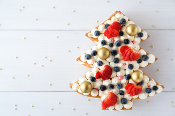 New Year's cake in the shape of a Christmas tree, decorated with golden balls, strawberries, blueberries and cream. Top view