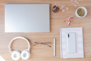Workspace with smatphone, glasses, wildflower, pen, washi tapes and paper clips on wooden background. Flat lay, top view