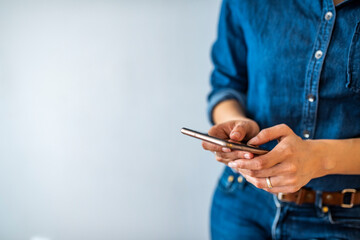 Young woman using cell phone to send text message on social network. Closeup of hands. Studio shot of an unrecognizable young woman using her cellphone against a grey background