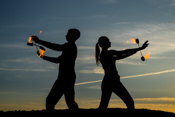 Couple of man and woman perform burning poi dance during fire performance in dark silhouettes
