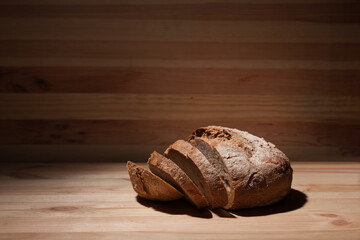Fresh handmade wheat bread cut into pieces on wooden background in the contrast light. horizontal frame side view with space area for text or design