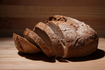 Fresh handmade wheat bread cut into pieces on wooden background in the contrast light. horizontal close-up frame side view