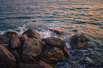 Obraz premium Orange sunset on the beach with big stones. Sunset on a rocky stone beach. Large stones with a beautiful texture against the background of a sea sunset. Evening landscape on the rocky sea shore.