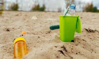 Small toy waste container on the sand beach with plastic garbage