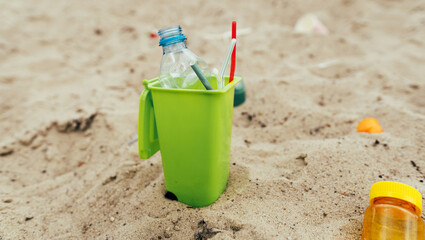 Small toy waste container on the sand beach with plastic garbage