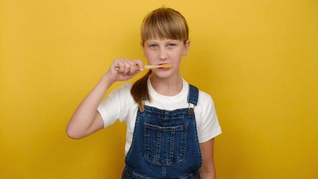 Oral health awareness concept. Portrait cute little caucasian blonde girl brush teeth, happy looking at camera, isolated over yellow color background in studio with copy space for promotion content