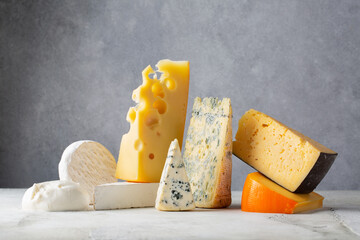 Different types of cheese. Cheeses mix maasdam, burrata, cheddar, dor blue, camembert, roquefort, brie on light grey background.