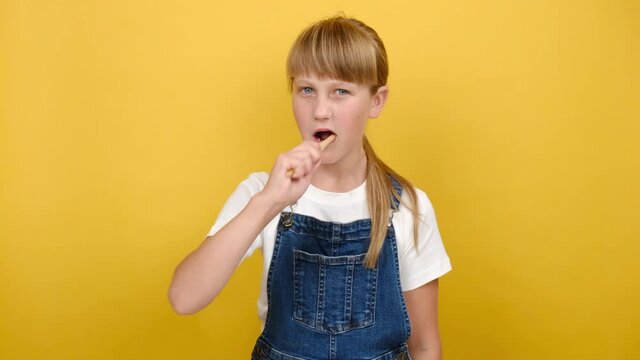 Portrait of smiling cute girl kid brushing teeth and show thumb up, happy looking at camera, posing isolated over yellow color background in studio. Oral care, self hygiene, daily habit concept