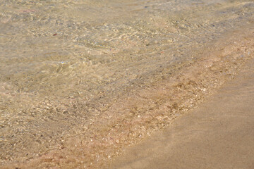 Clear waves and colorful sand on tropical sandy beach in Crete Greece.