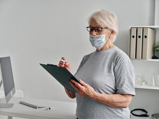 elderly woman with documents in hands in the doctor's office medical mask covid-19 passport