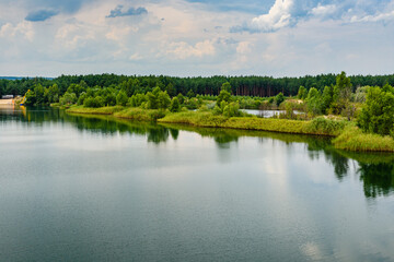 Fototapeta na wymiar View on a lake in the abandoned sand quarry and dramatic sky