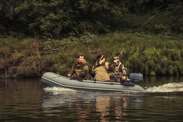 Fishermen sailing on inflatable motor boat along river bank and fishing with fishing rods  