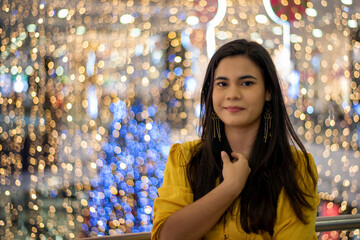 Beautiful brown haired brunette Spanish woman in yellow dress at a mall during the holiday season with Christmas lights in the background