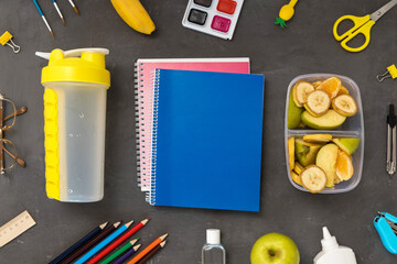 A school lunch box with a water and fruit on a grey background. School supplies, stationery, and food. Flatly. From above. the concept of healthy eating.