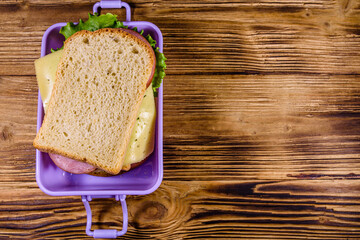 Lunch box with sandwiches on a wooden table. Top view