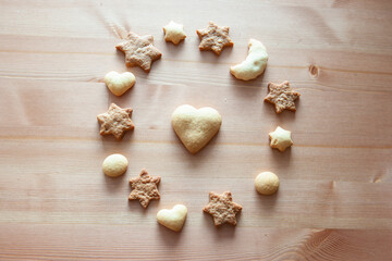 Different figures of ginger biscuits on a wooden table. Christmas cookies, star figures, heart figures, moon figure, and big heart is in the center