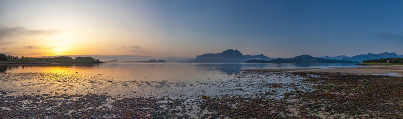 Naklejka premium Panoramic view from beach of the setting sun on Amnesvika bay with mountains on the horizon. Island Amnoya. Norway