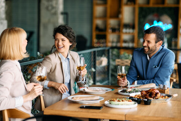 Group of happy co-workers laugh and talk while having lunch together at restaurant.