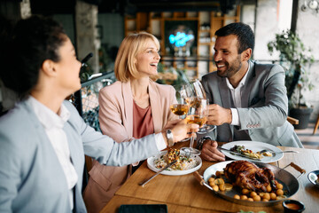 Cheerful business colleagues toast with wine during lunch in restaurant.