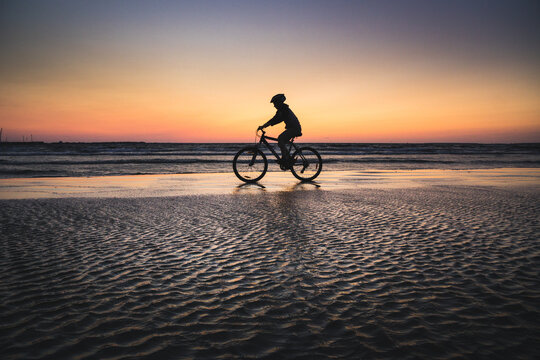 Silhouette of a boy on a bicycle riding on a small portion of sand in the middle of the water from the baltic sea. Dramatic stunning sunset colors. Estonia, Europe - Powered by Adobe