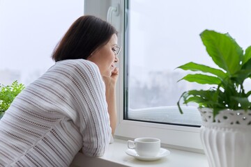 Winter season, snow, middle aged woman looking at home window