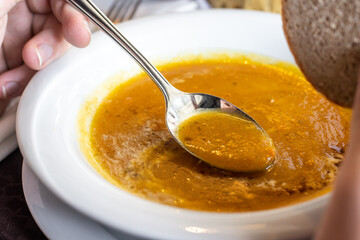 Roasted pumpkin and carrot soup. Person eating with spoon.
