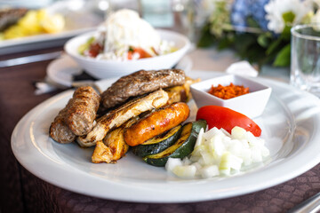 Mixed meat plate with cevapcici, grilled pork, sausage, and onions. Traditional Balkan dish. Delicious barbecue cuisine.