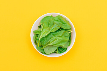Fresh Baby Spinach Leaves in White Bowl on Yellow Background - Top View. Vegan and Vegetarian Culture. Raw Food, Green Leaves. Healthy Diet