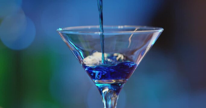 Professional barman decorates a blue cocktail with ice  . Bartender prepares cocktails on defocused background and pours and serves a cocktail . Barman preparing colorful cocktail . Slow Motion .