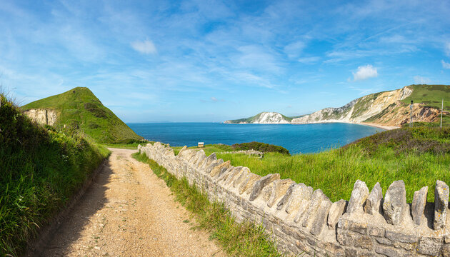 Gravel path from Tyneham village leading to Worbarrow Bay and Jurassic cliffs with old stone wall on a bright summers day. Used by the army for training & target practice. Tyneham, Wareham, Dorset, UK